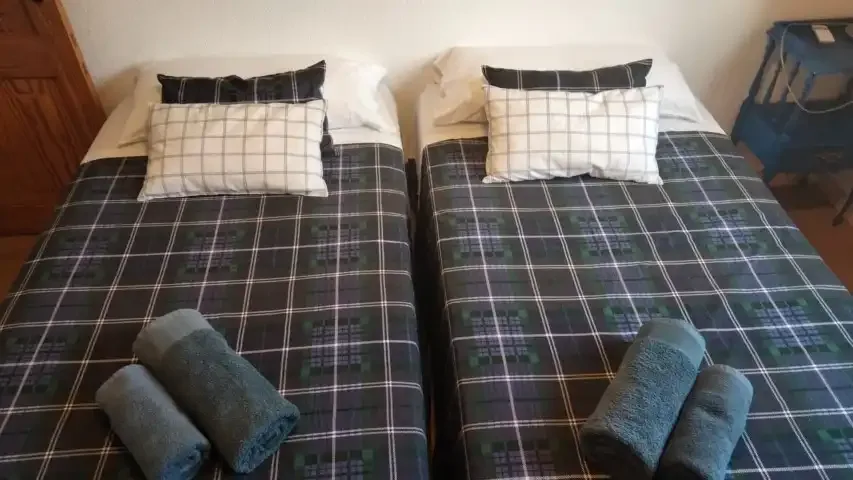 A bedroom with two beds covered in dark plaid bedding and folded towels.