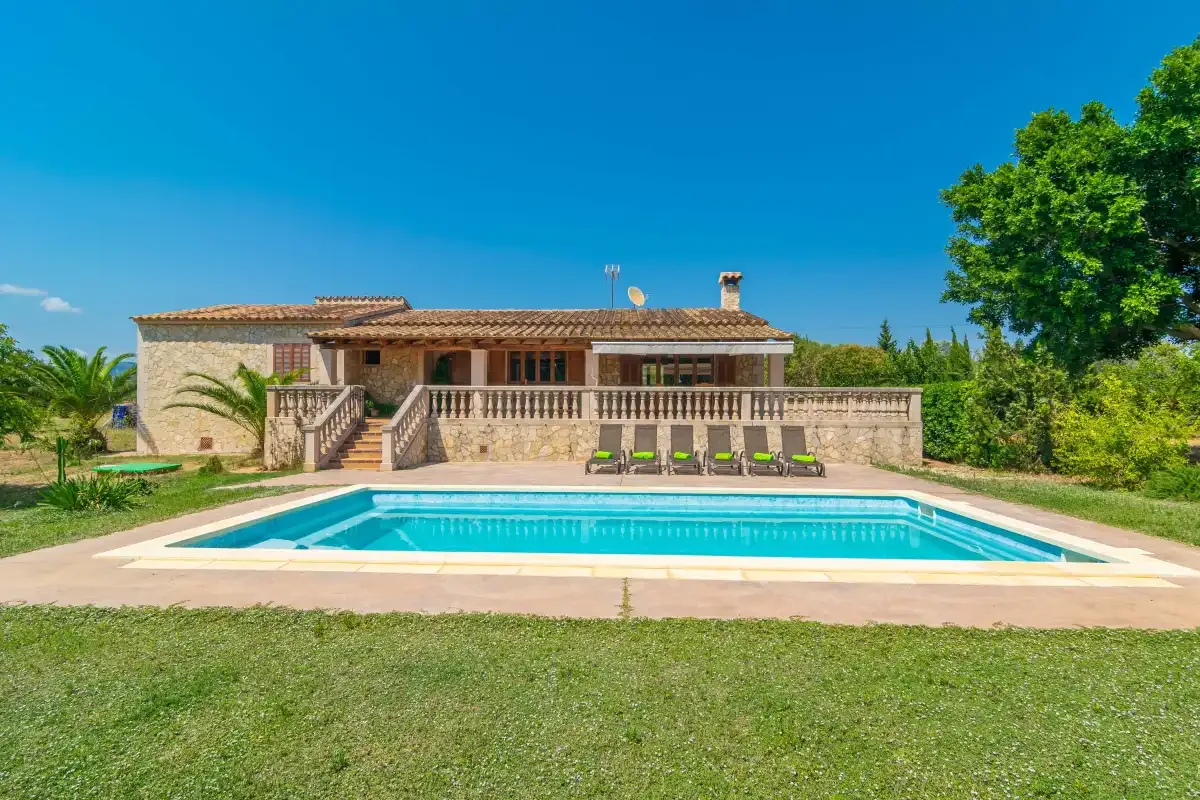 A swimming pool sits in front of a single-story house with a covered terrace.