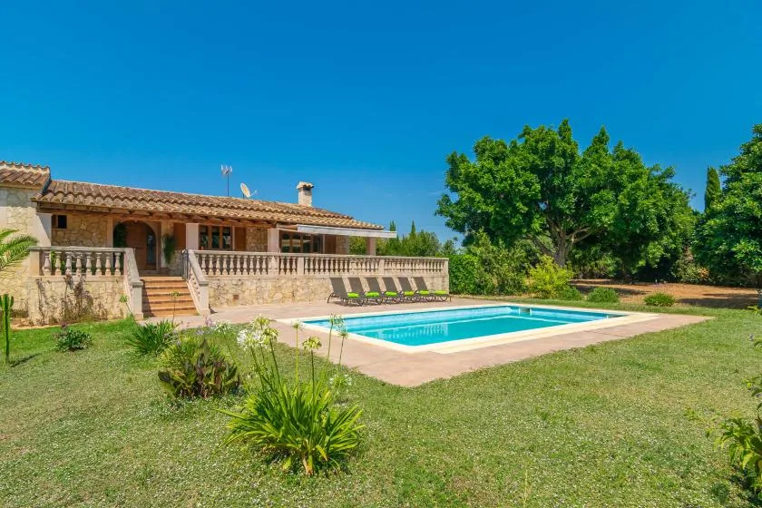 A swimming pool sits in a grassy yard beside a stone house.