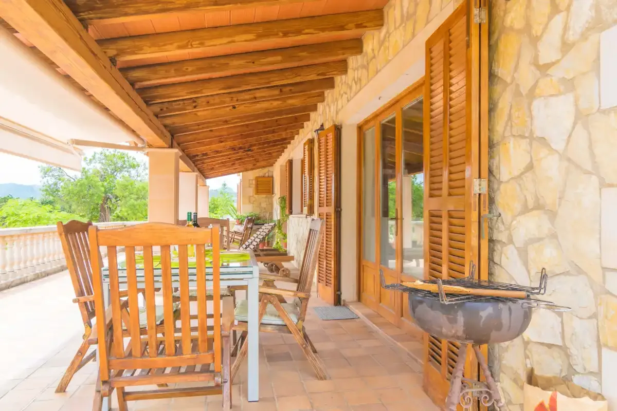 A covered outdoor dining area with wooden tables and chairs beside the house.