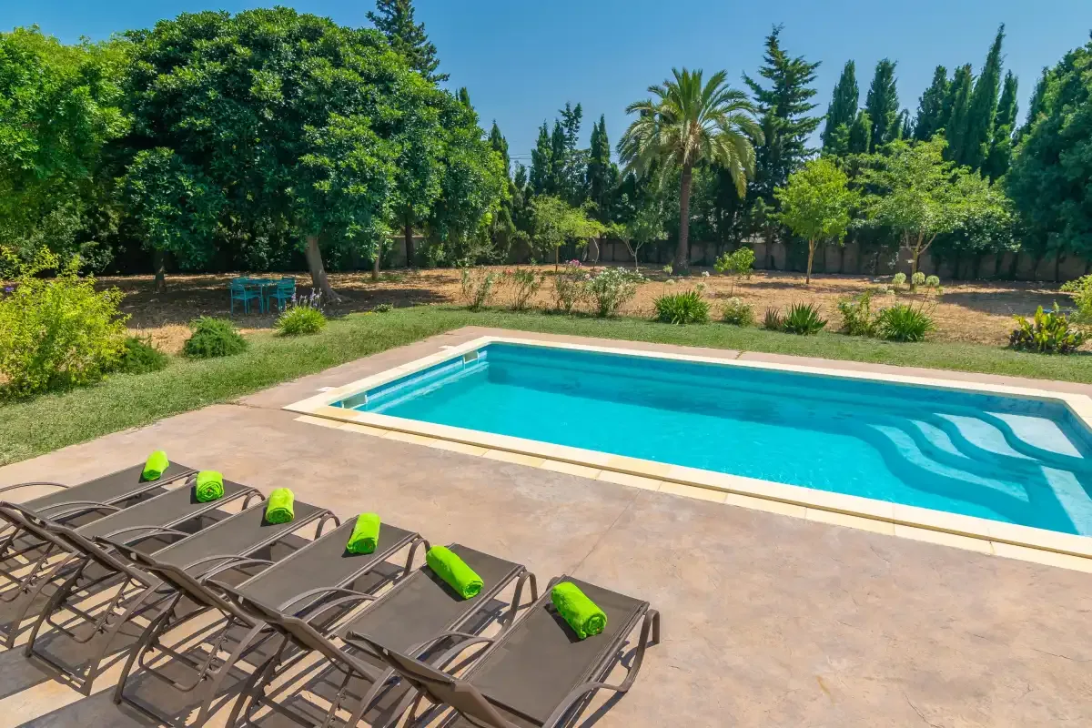 A swimming pool and sun loungers sit beside a tree-lined garden.