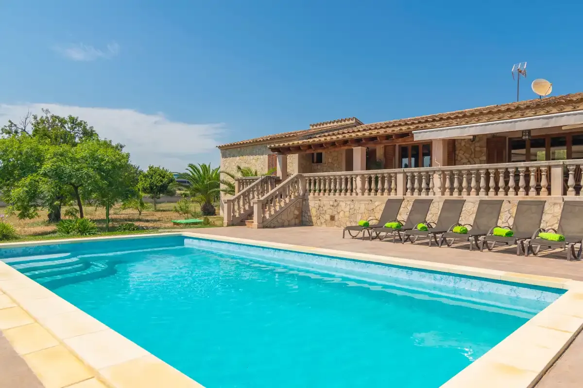 A swimming pool beside a stone house, with lounge seating along the patio.