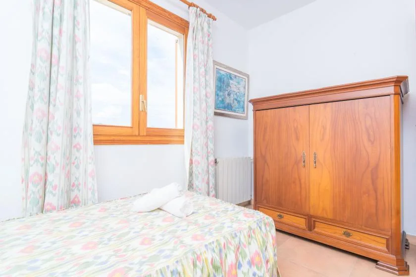 A bedroom with a bed beside a wooden wardrobe and a window.