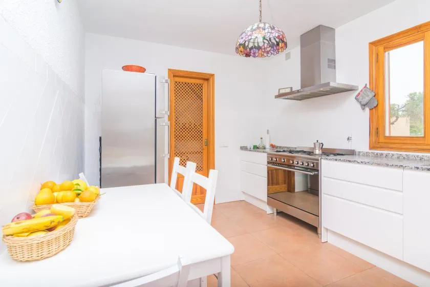 A bright kitchen with a dining table, refrigerator, and cooking range.