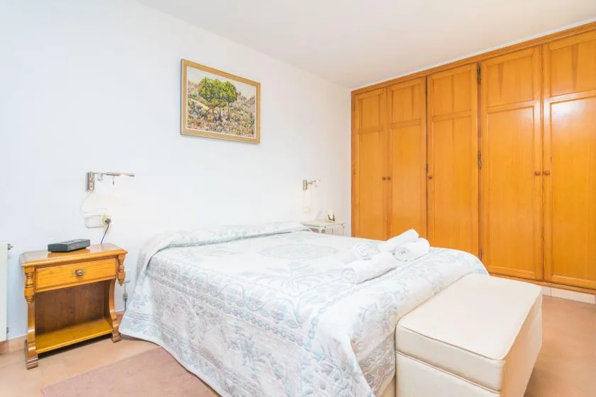A bedroom with a bed beside wooden wardrobes and a small bedside table.