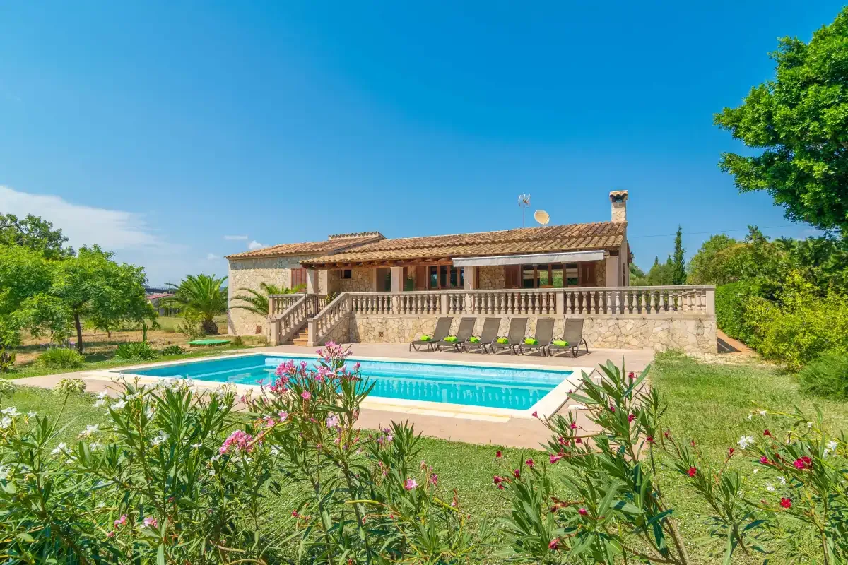 A swimming pool and landscaped garden sit in front of a low tiled-roof building.