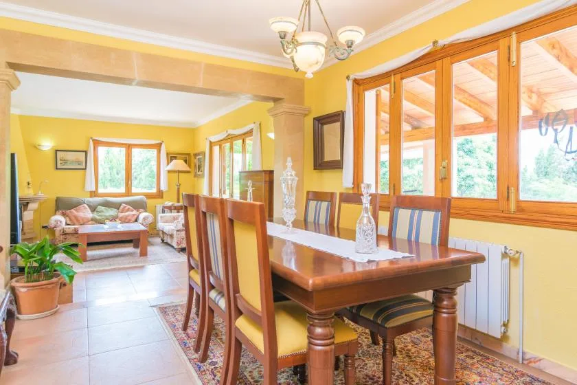 A dining area with a wooden table and chairs beside large windows.