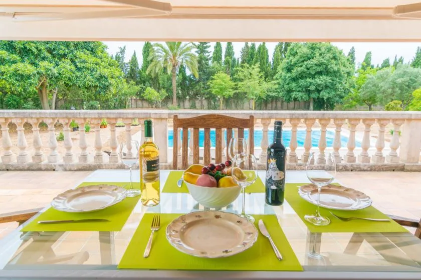 A dining table with plates and fruit sits on a terrace overlooking a garden.