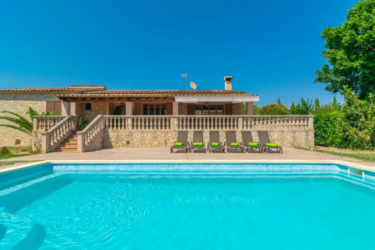 A swimming pool in front of a stone house with outdoor seating.