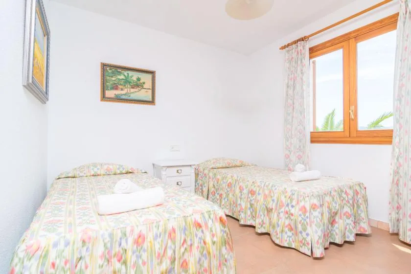 A bright bedroom with two beds dressed in colorful floral bedding.
