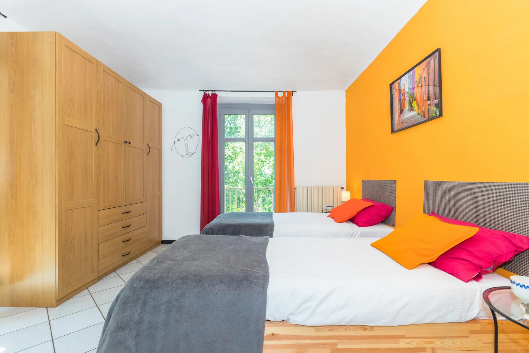 A bedroom with two beds, wooden wardrobes, and a bright orange accent wall.