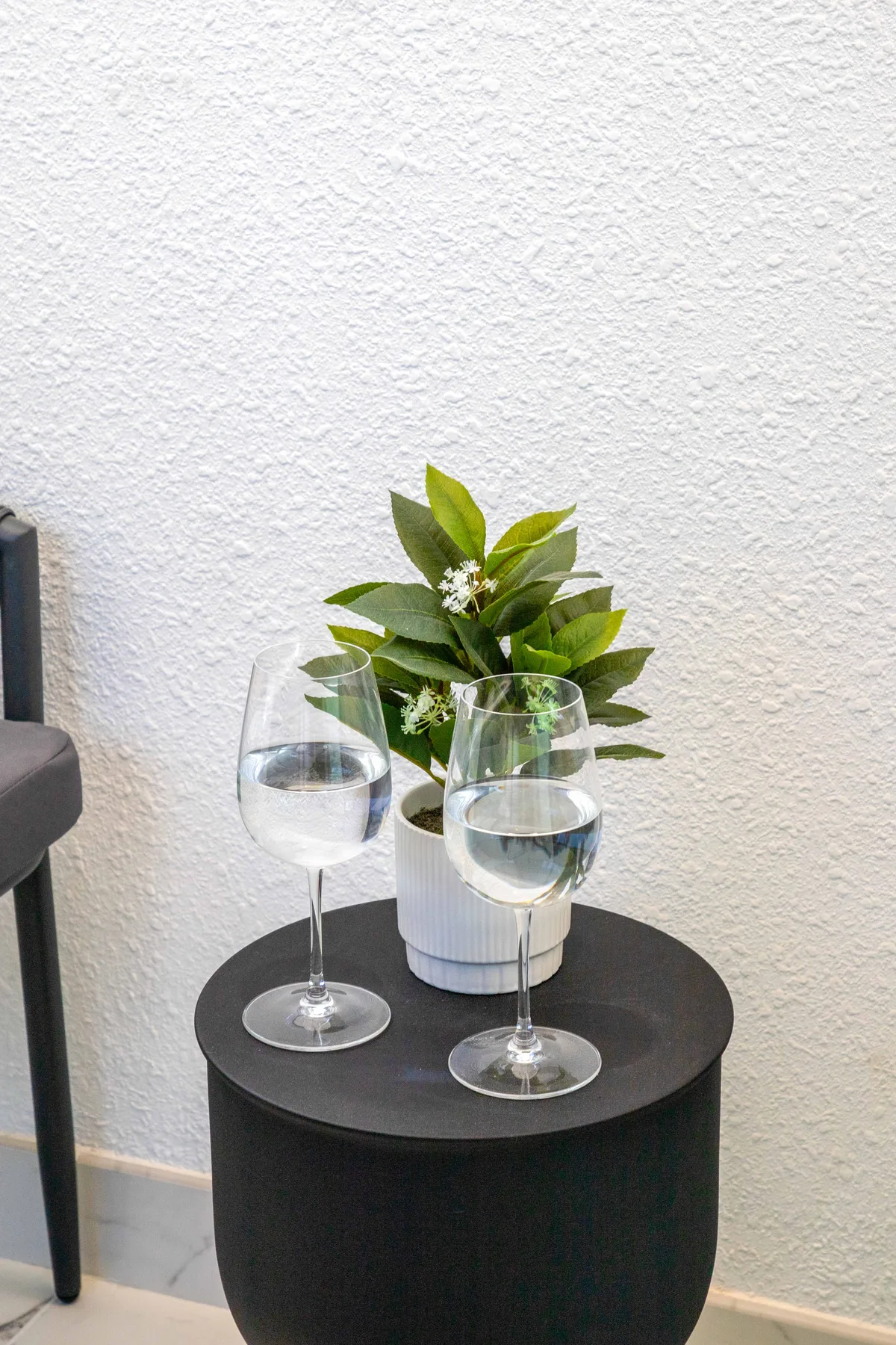 Una mesa redonda pequeña sostiene dos copas de agua y una planta frondosa.