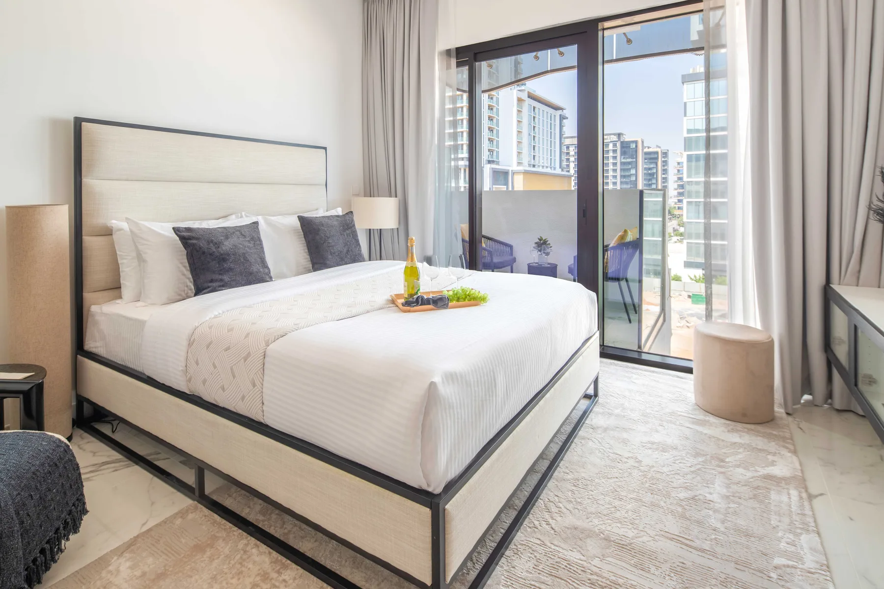 Un dormitorio luminoso tiene una cama bien hecha junto a ventanas de piso a techo.