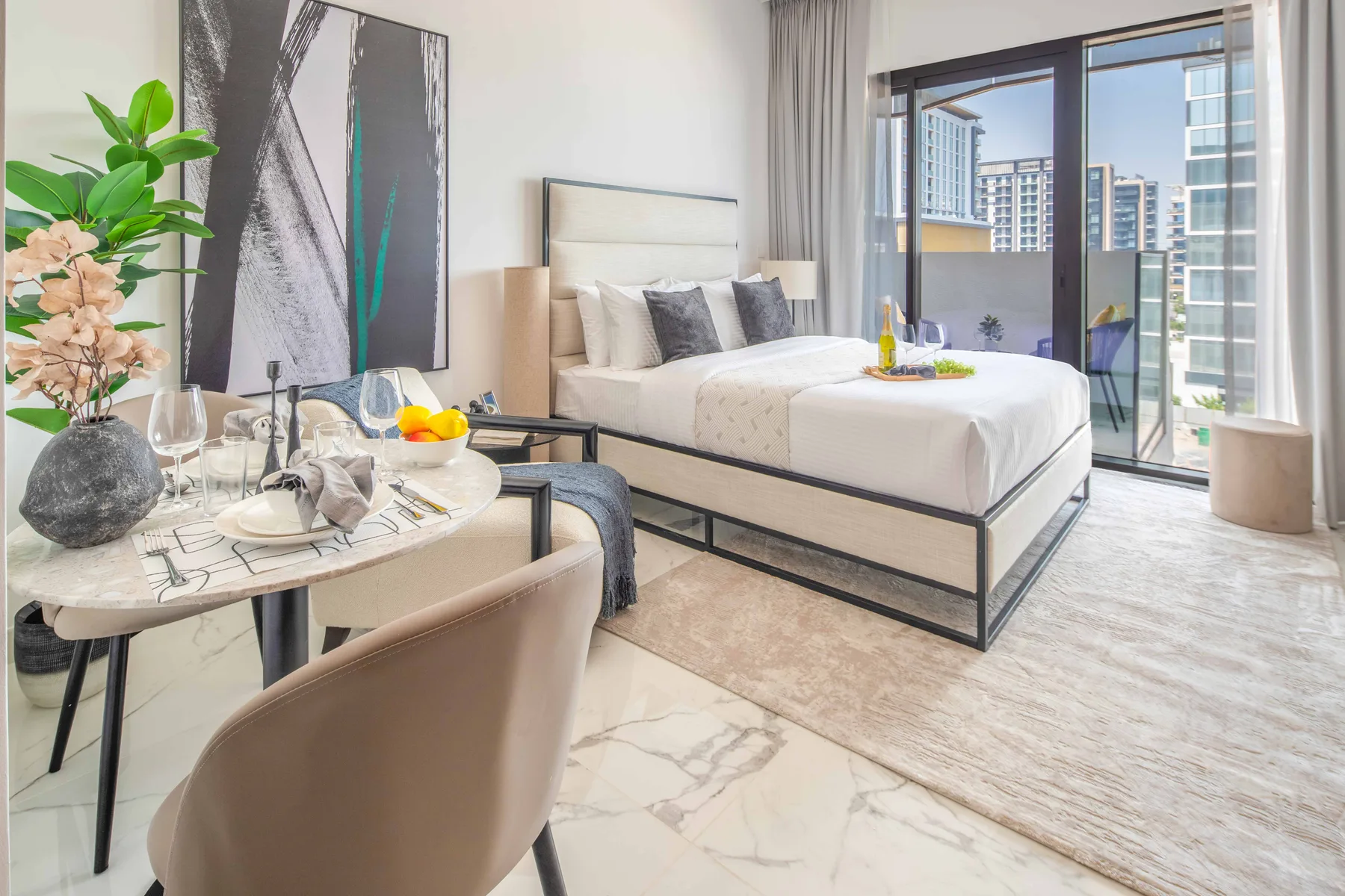 Un dormitorio luminoso con una cama, una mesa pequeña y ventanales.