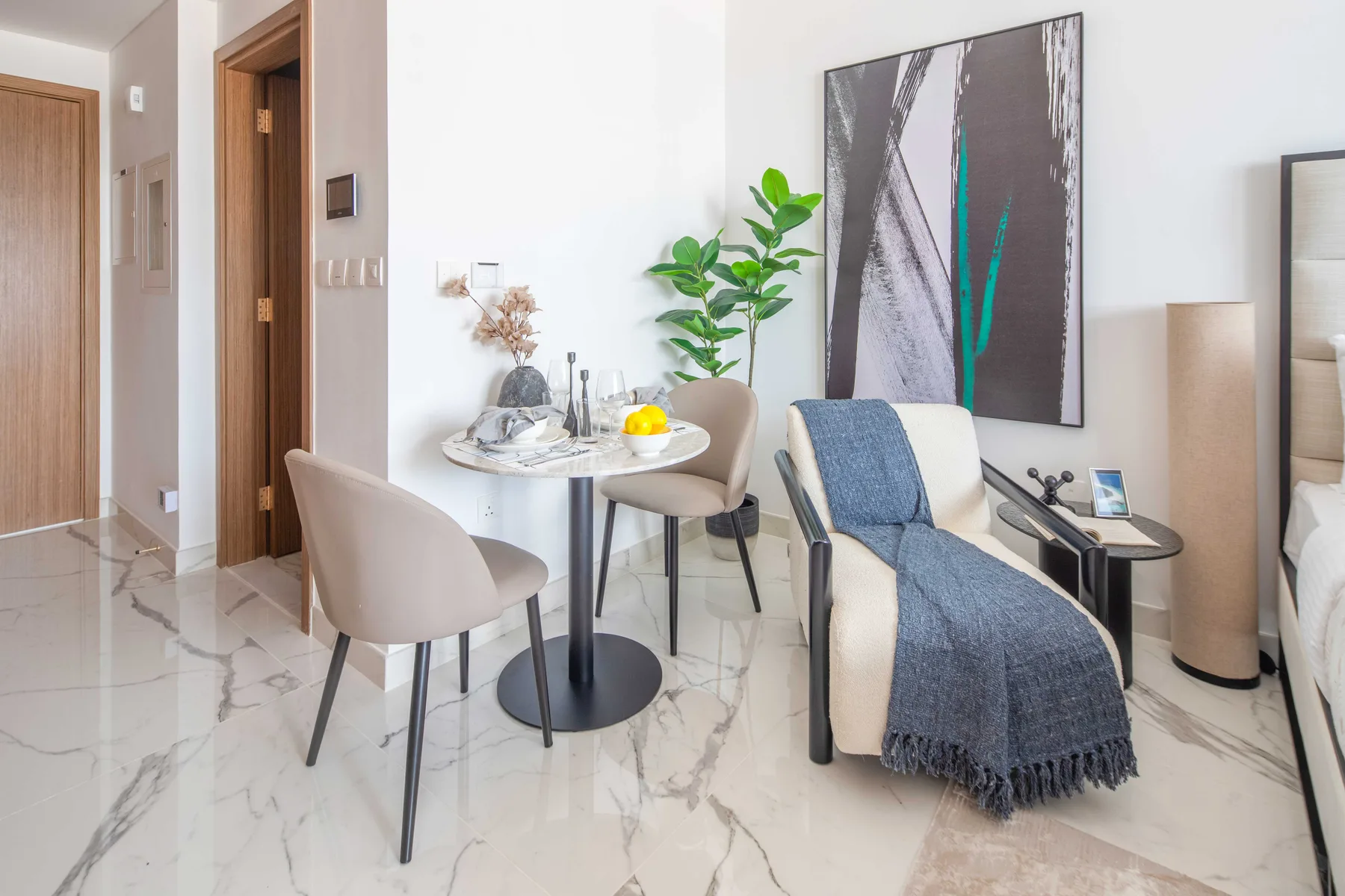 Una luminosa zona de estar tiene una pequeña mesa de comedor, asientos tapizados y una planta frondosa.