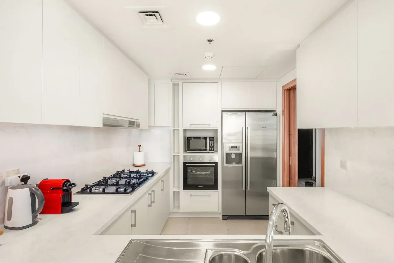 A bright kitchen with white counters, a cooktop, and stainless steel appliances.