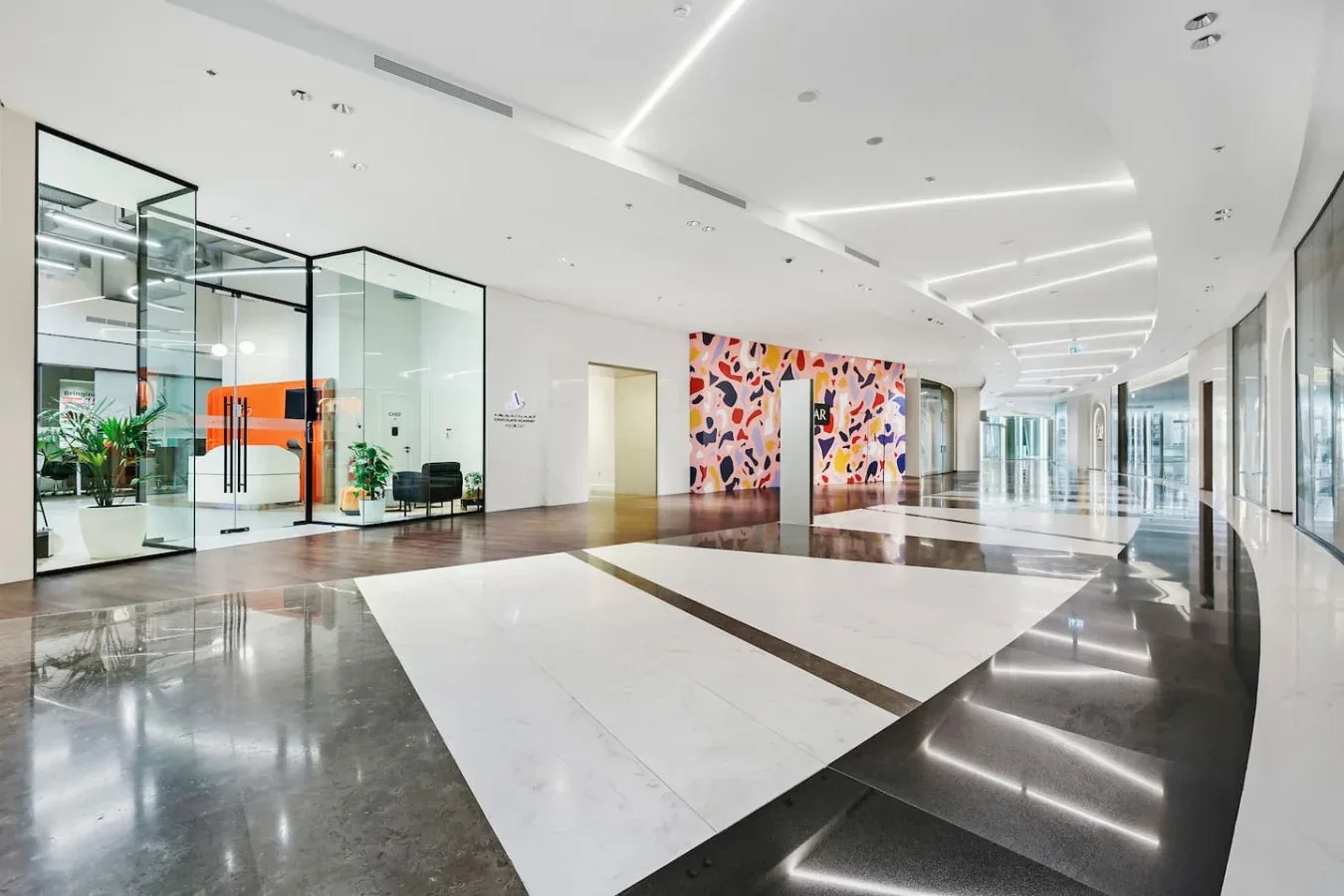 A bright modern lobby with glass-walled rooms and colorful wall art.