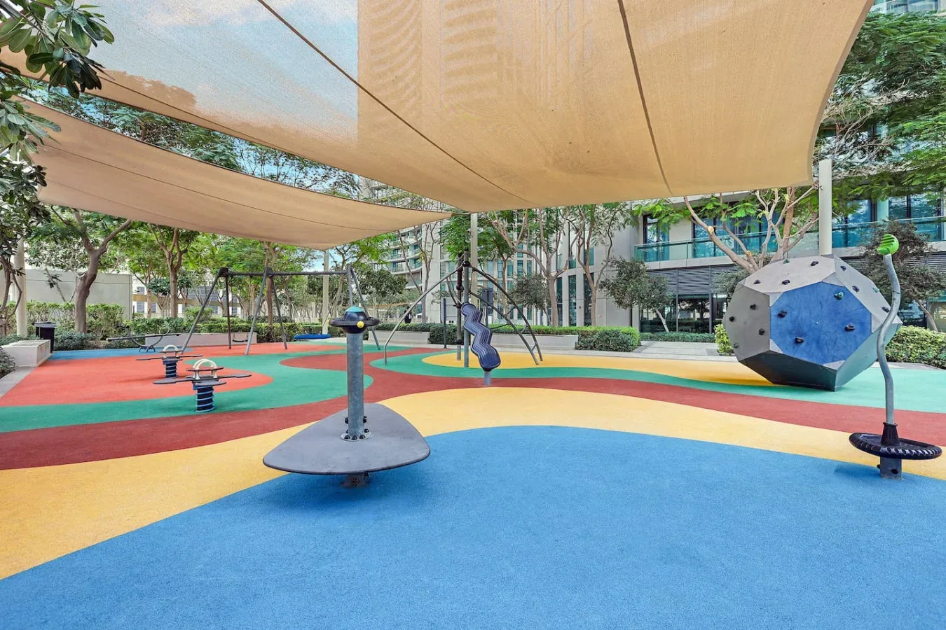 A colorful playground with climbing equipment sits beneath large shade canopies.