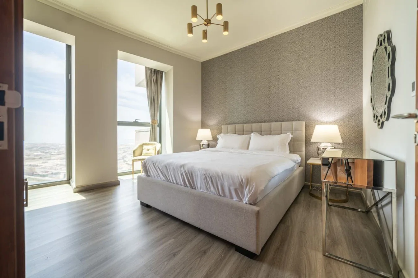 A bright bedroom features a large bed, bedside tables, and tall windows.