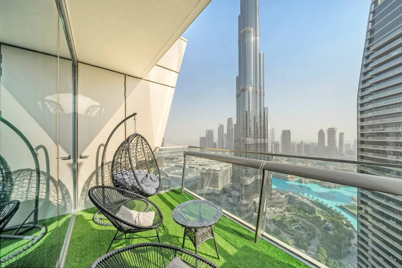 A balcony seating area overlooks a city skyline, with a glass railing and green flooring.
