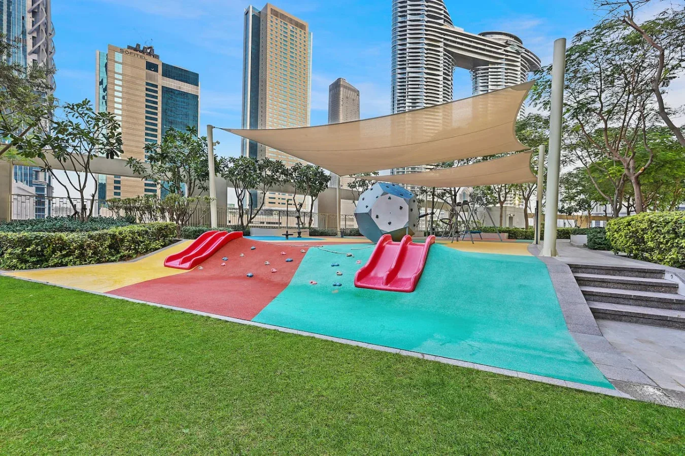 An outdoor playground with colorful climbing and sliding equipment beneath a shade canopy.