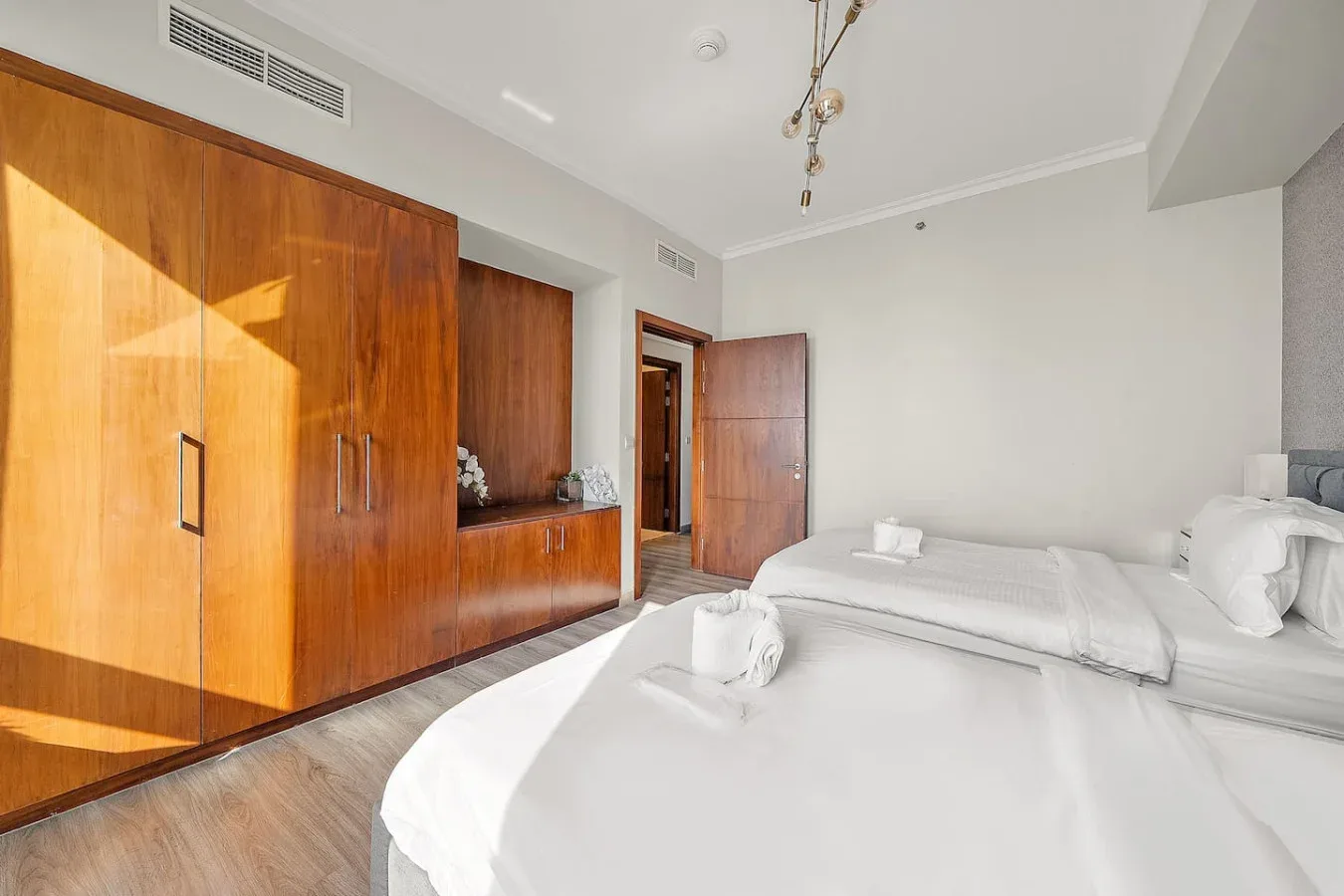 A bright bedroom with white bedding and a large wooden wardrobe.
