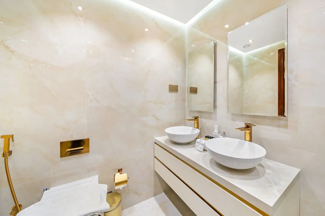 A bright tiled bathroom has a long vanity with two sinks and large mirrors.