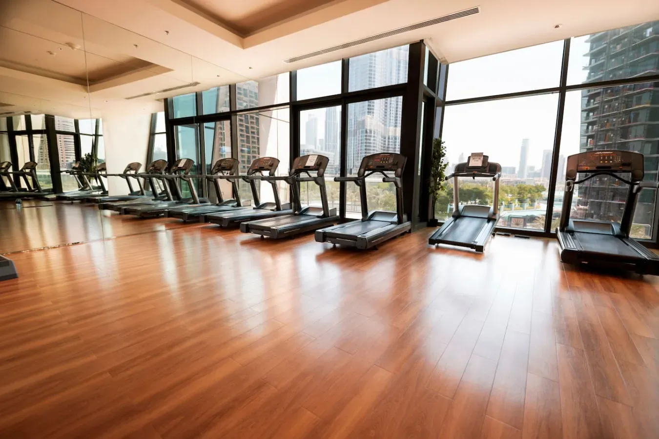 A gym with treadmills arranged beside large windows.