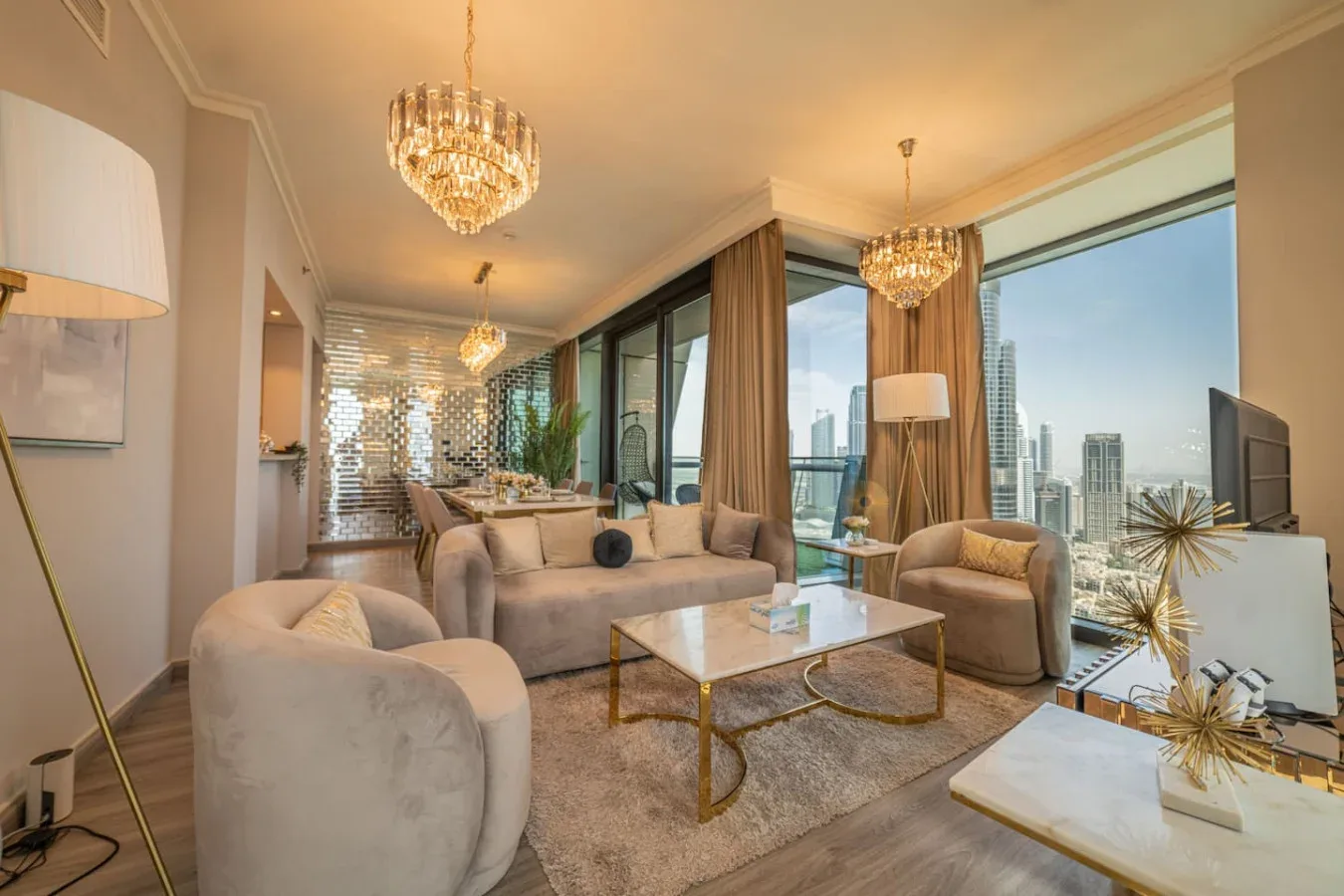 A bright living room with seating, a coffee table, and floor-to-ceiling windows overlooking the city.