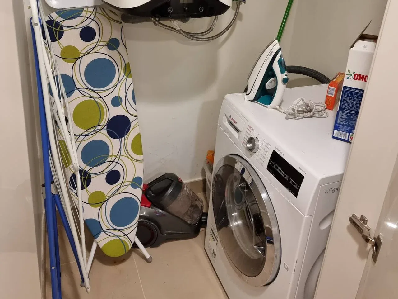 A laundry area with a front-loading washing machine and an ironing board.