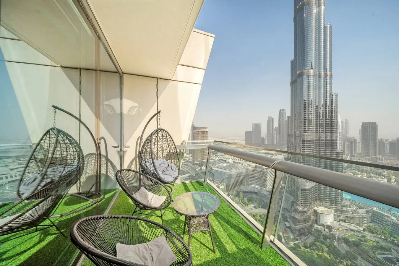 A balcony seating area with woven chairs overlooks a city skyline.