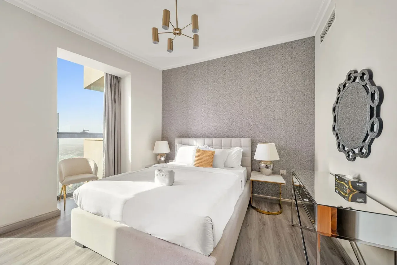 A bright bedroom has a white bed, bedside lamps, and a balcony doorway.