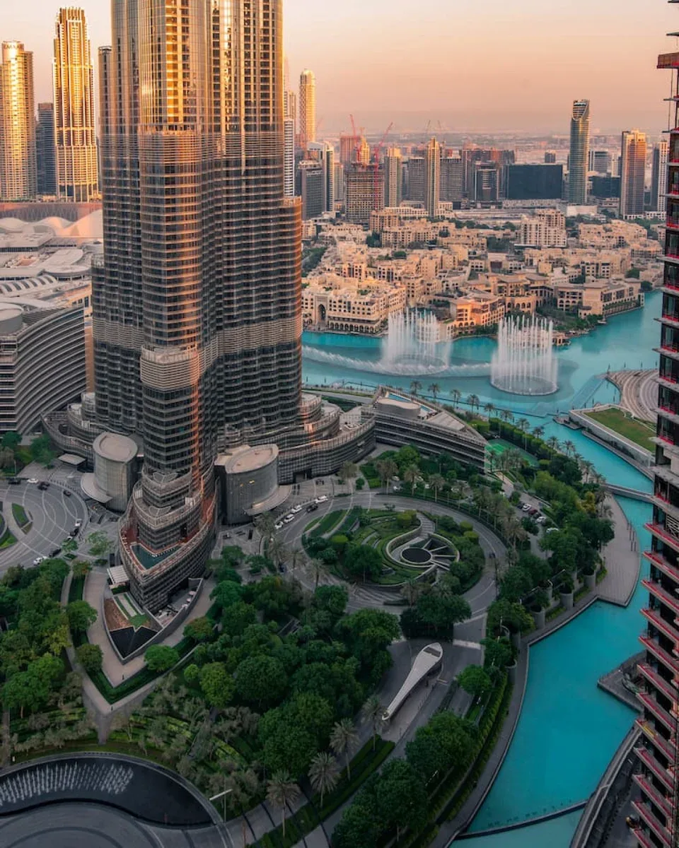A city skyline overlooks a turquoise waterfront and landscaped park.