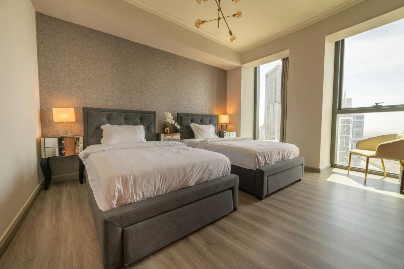 A bedroom with two beds, bedside tables, and large windows.