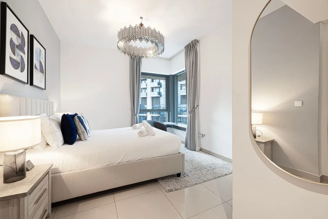 A bright bedroom with a white bed, framed artwork, and large windows.