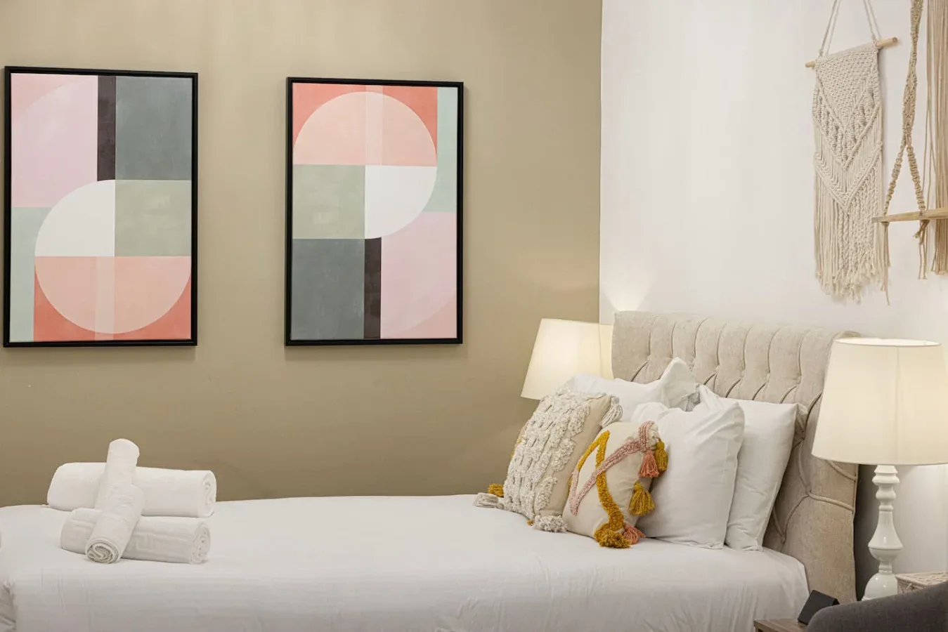 A neatly made bed sits beneath two colorful abstract prints.