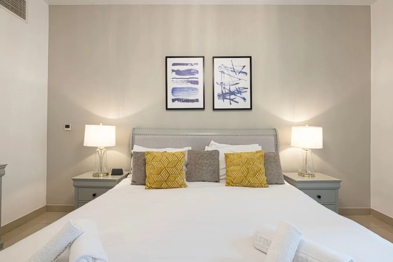 A bedroom with a neatly made bed, bedside tables, and two framed prints above the headboard.
