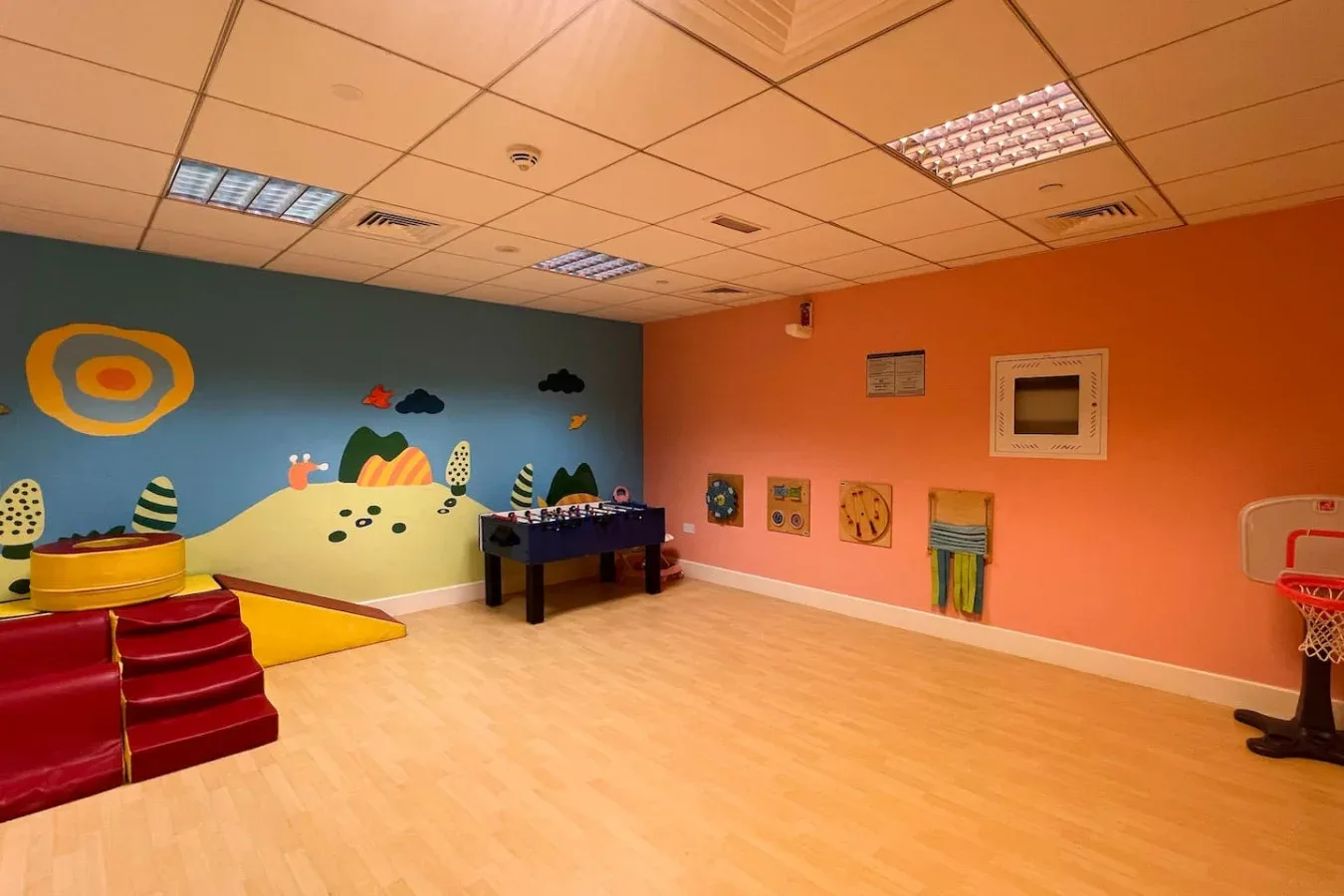 A colorful indoor playroom with a painted wall mural and children's play equipment.