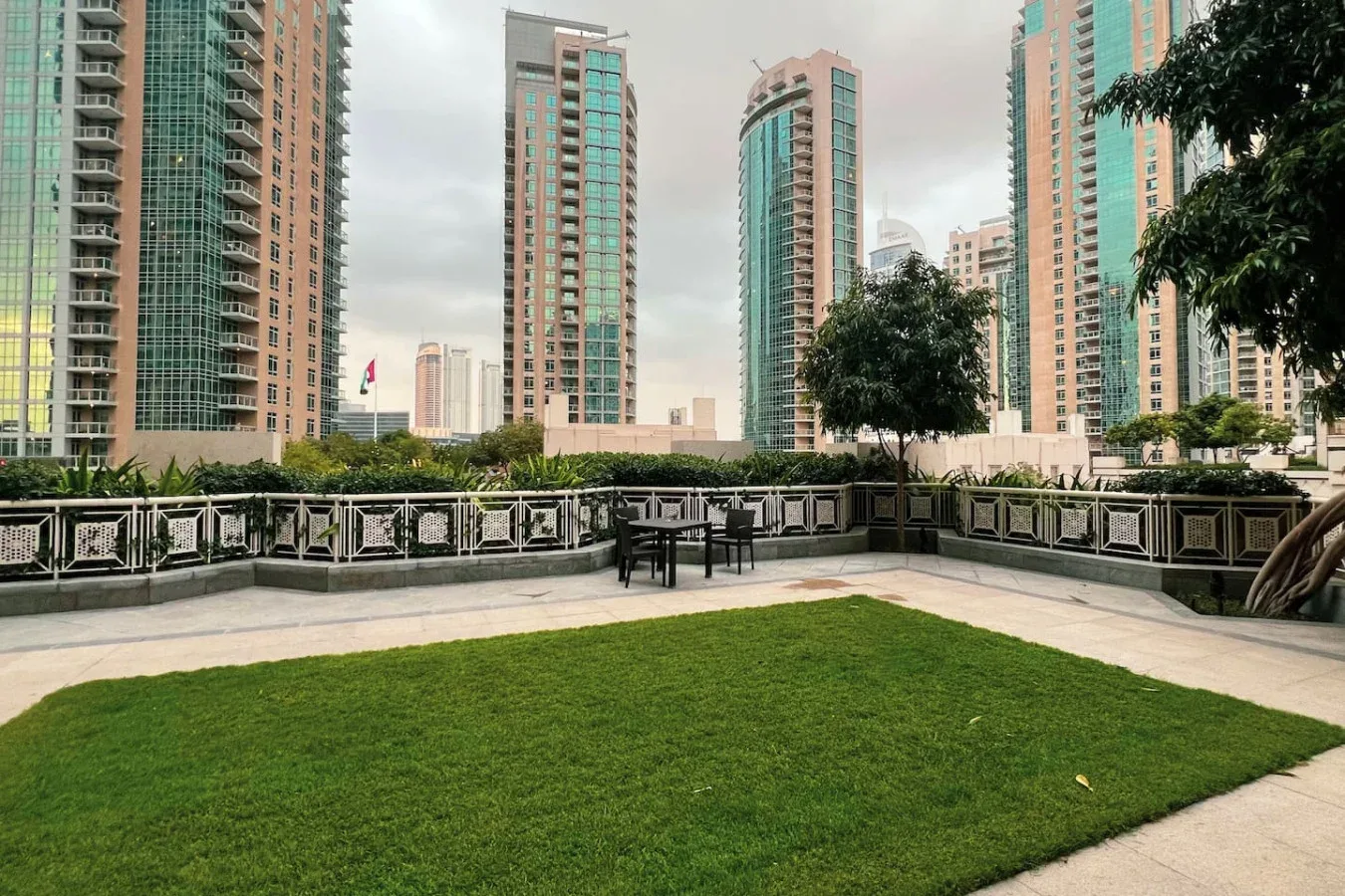 An outdoor terrace with a lawn and seating, surrounded by tall buildings.