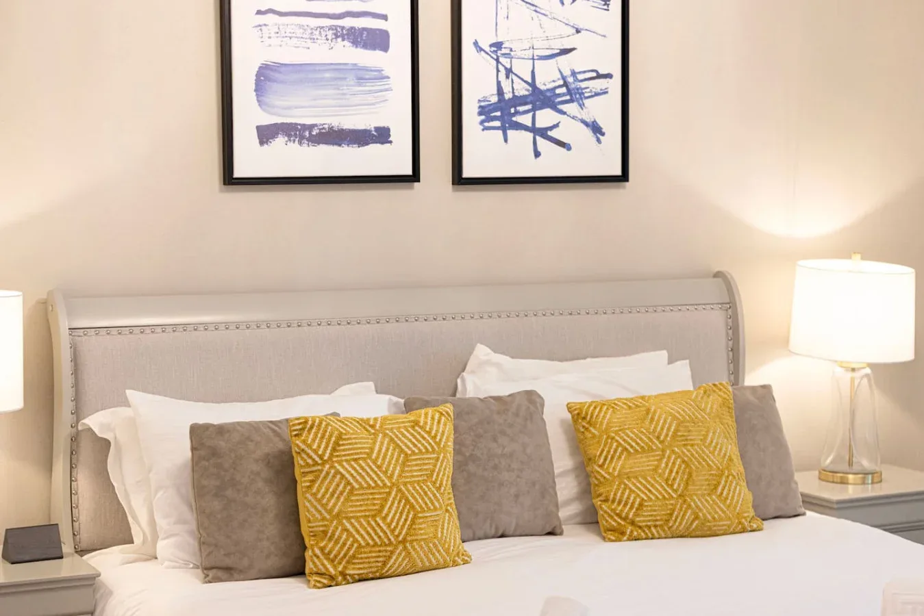 A bedroom with a neatly made bed and framed abstract artwork above the headboard.