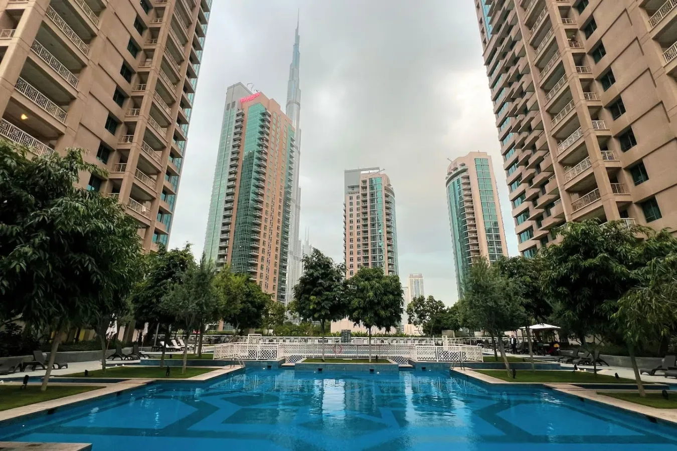 A swimming pool sits among landscaped grounds and tall residential buildings.