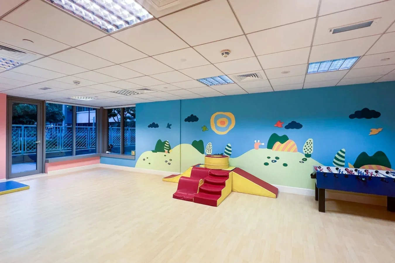 A bright indoor playroom has a colorful mural and a small play structure.
