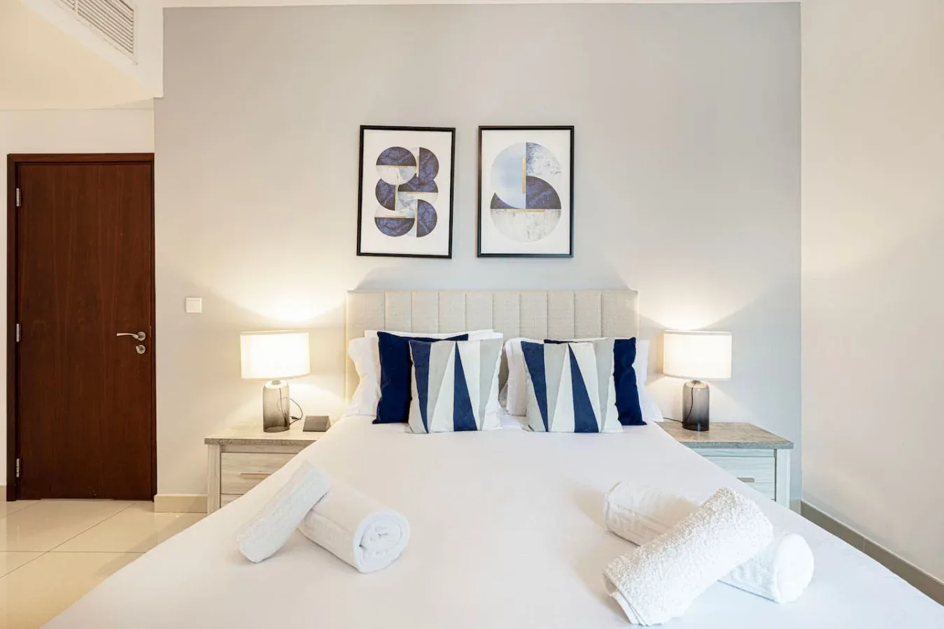 A bedroom with a neatly made bed and two framed prints above the headboard.