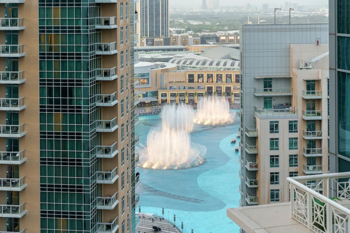 A swimming pool with fountain jets is visible between high-rise buildings.