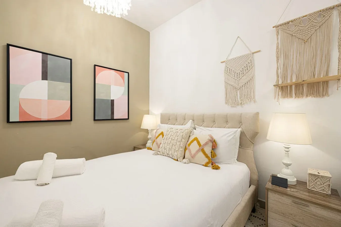 A bedroom with a neatly made bed, patterned pillows, and framed abstract art.