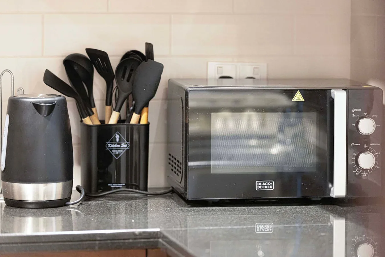 A kitchen counter with a toaster oven, electric kettle, and utensils.