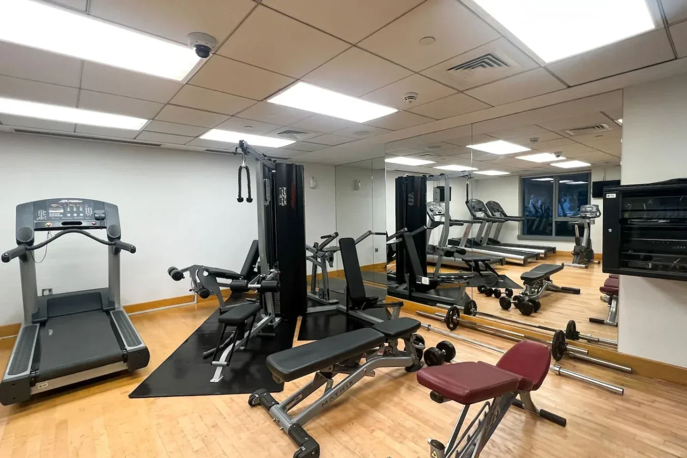 A fitness room with exercise machines, weight benches, and a mirrored wall.