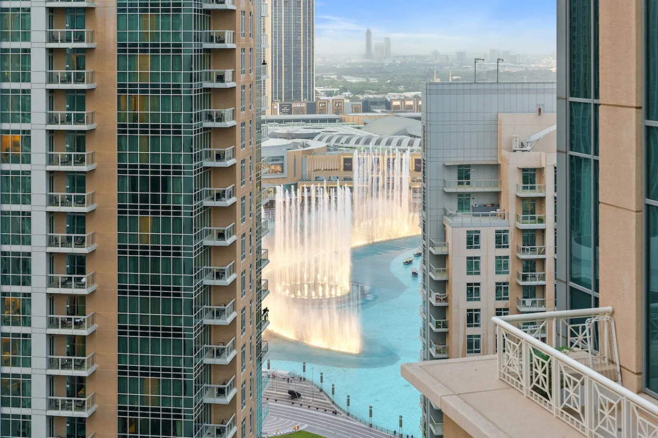 A city view between high-rise buildings overlooks a turquoise pool and illuminated fountains.