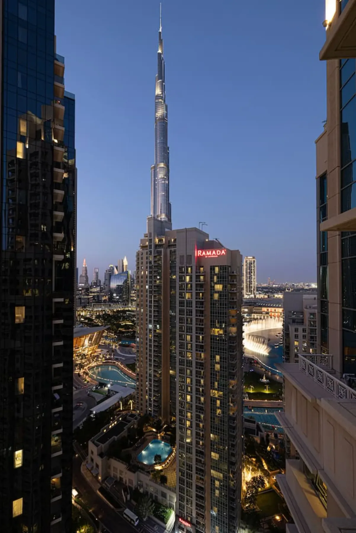 A city skyline at dusk features a tall, slender tower rising above surrounding buildings.
