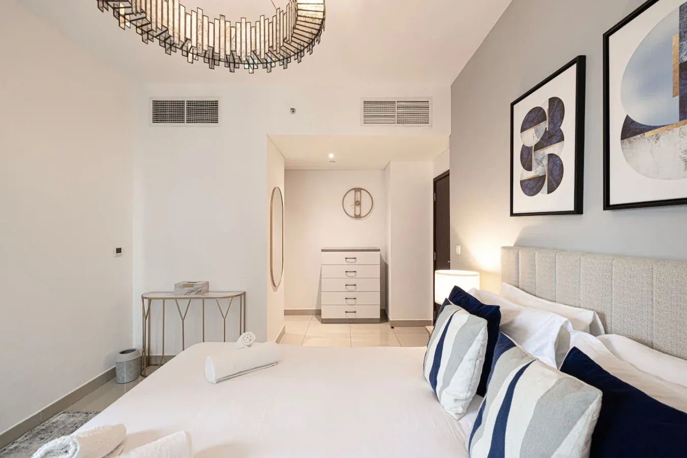 A bright bedroom with a bed, abstract wall art, and a dresser in the background.